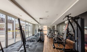 A gym with cardio machines, weightlifting equipment, and a large window providing natural light. - Comfort With Pool in Aguas Claras Sht1701 (Águas Claras)