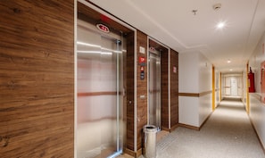 A hotel corridor with two elevators, wooden paneling on the walls, a fire extinguisher, and a trash bin. - Studio With Pool in Aguas Claras Sht1701 (Águas Claras)