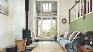 A cozy living room with a stone fireplace, a blue sofa, a wicker basket, and a green wall. - Jackson s Barn in Water Yeat (Ulverston)