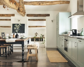 A modern kitchen with exposed wooden beams, a dining area with a rustic table, and a view of the living room. - Jackson s Barn in Water Yeat (Ulverston)