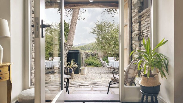 A doorway leading to an outdoor patio with stone flooring, a table, chairs, and a potted plant. - Jackson s Barn in Water Yeat (Ulverston)
