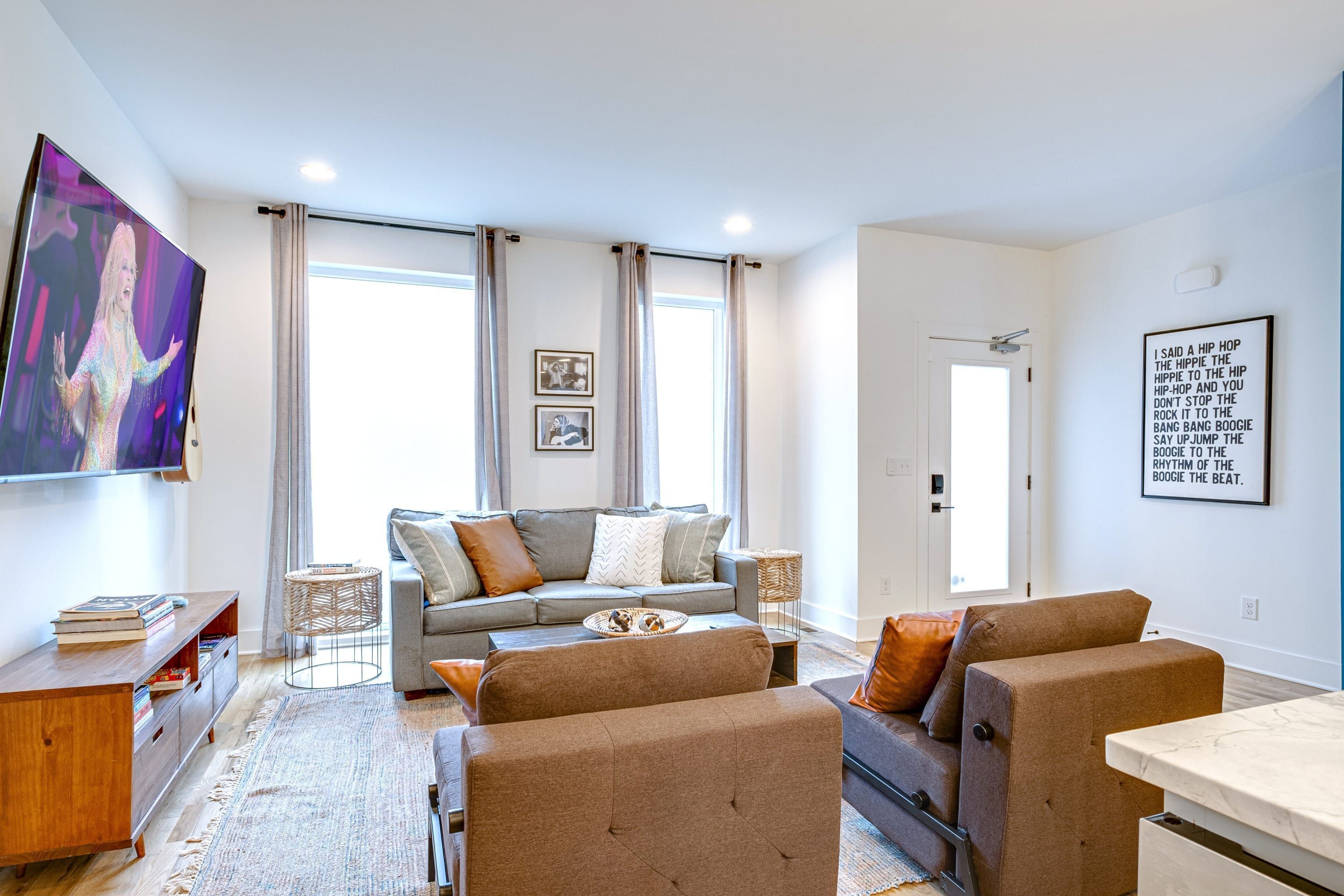 Ein modernes Wohnzimmer mit einem grauen Sofa, braunen Sesseln, einem Couchtisch und einem wandmontierten Flachbildfernseher.