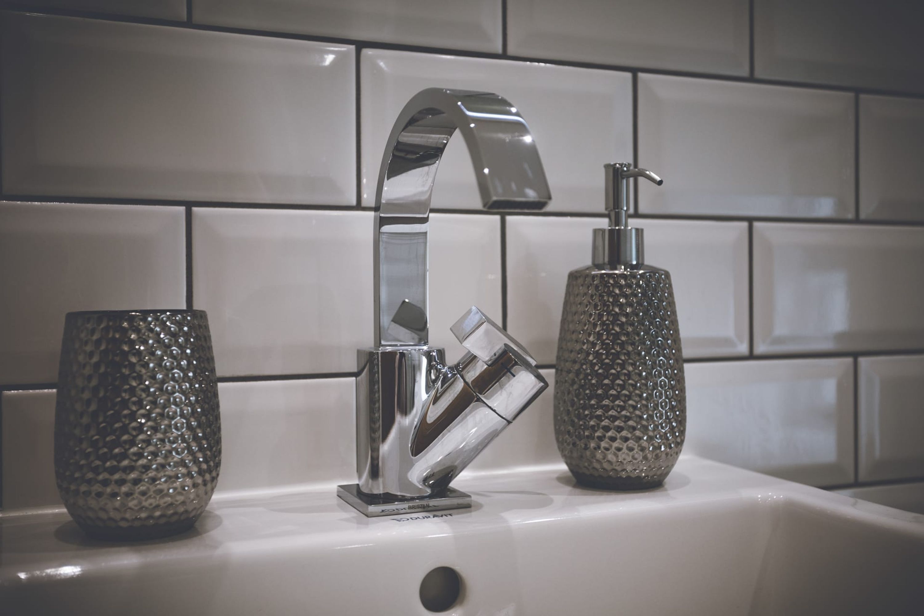 Een wastafel met een chromen kraan en twee dispensers voor zeep.
