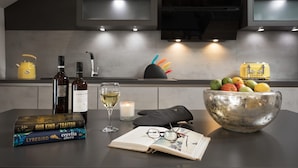 Eine moderne Küche mit einer großen Kochinsel, einer Weinflasche, einem Glas Weißwein, einer Kerze, einer Obstschale und einem Buch.