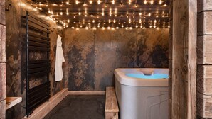 Ein Wellnessraum mit einer hölzernen Sitzbank, einem aufgehängten weißen Handtuch und einer Whirlwanne.