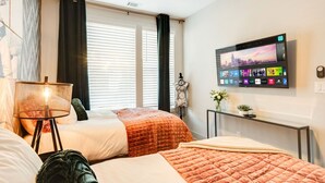 Camera d'albergo con due letti, una TV a parete, un comodino con lampada e una finestra con persiane.