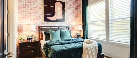 Un dormitorio con una cama, mesitas de noche, una ventana con persianas y un papel tapiz estampado.