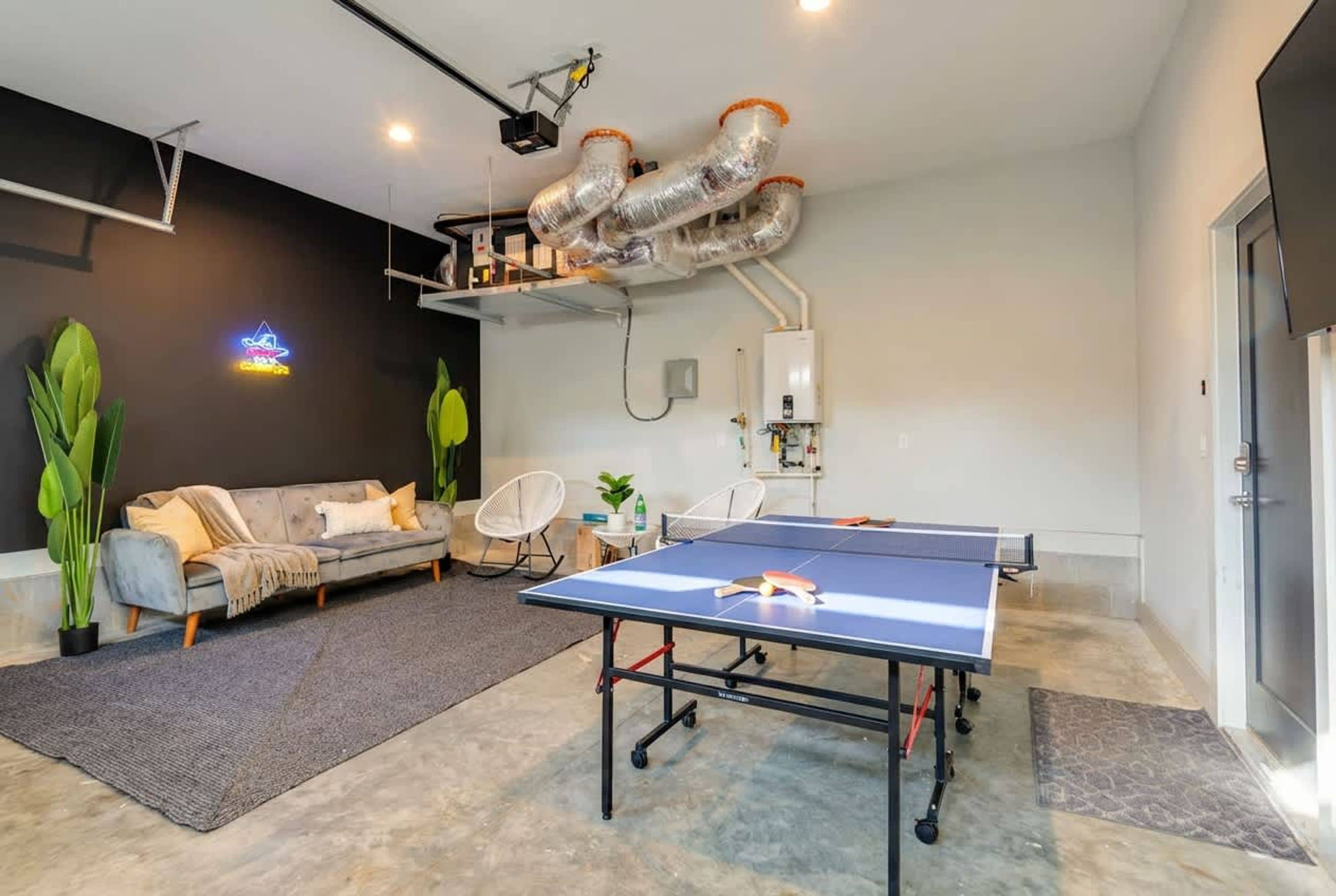 A room with a ping pong table, a sofa, chairs, and a neon sign.