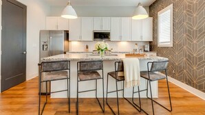 Una cucina moderna con mobili bianchi, un'isola centrale con sgabelli da bar, un frigorifero in acciaio inossidabile e luci a sospensione.