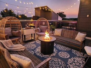 An outdoor seating area with wicker furniture, a fire pit, and string lights. - Rooftop Views Ping Pong Lounge Near Downtown Nashville (Nashville)