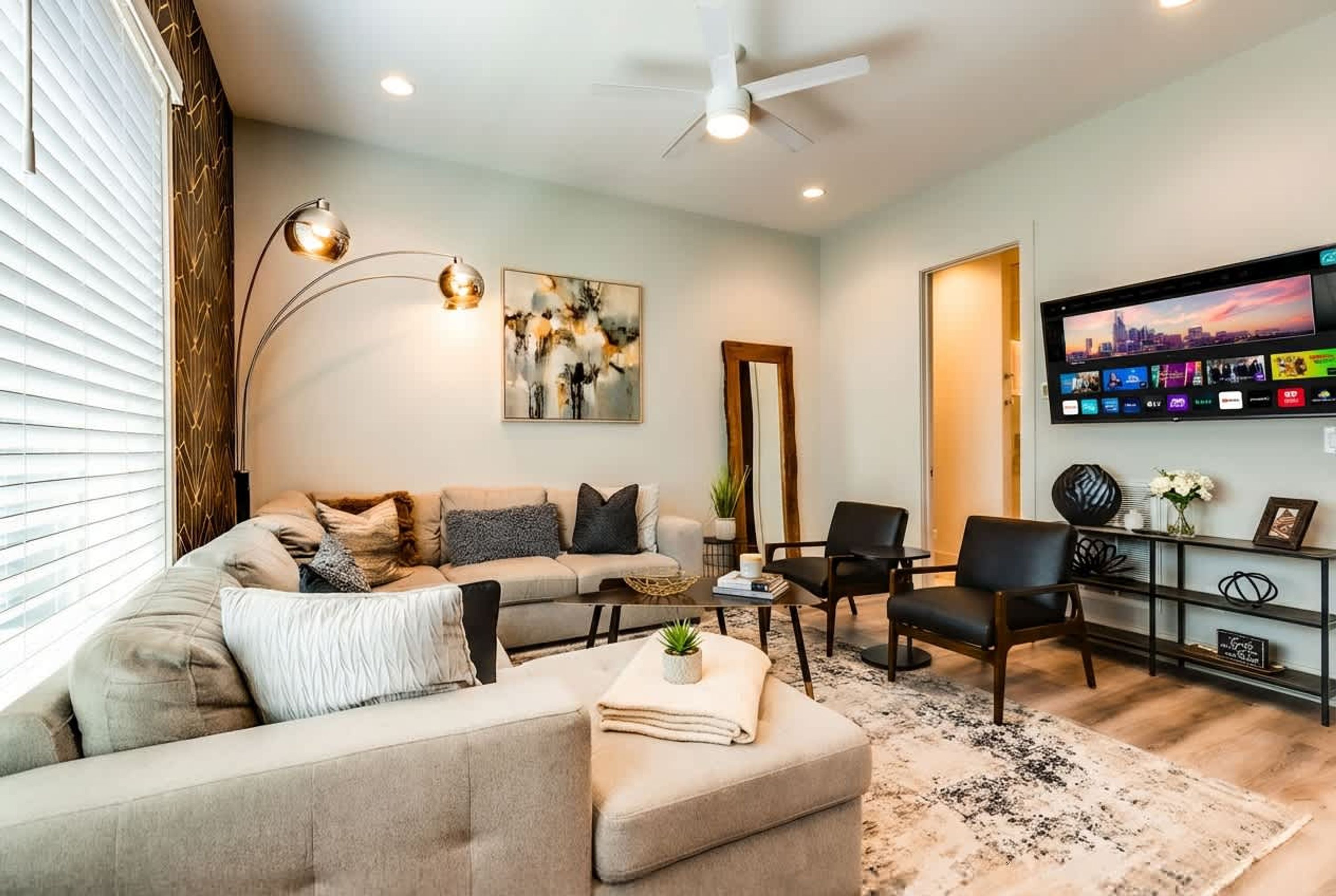 A modern living room with a sectional sofa, a coffee table, a TV mounted on the wall, and a ceiling fan.