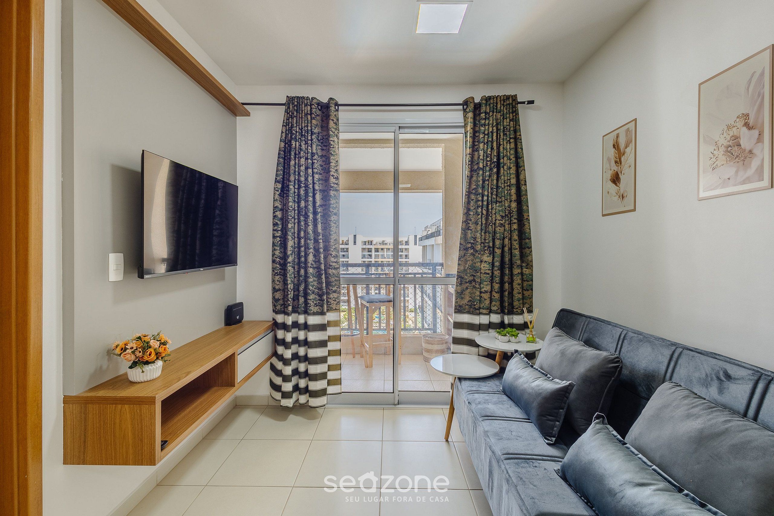 Een woonkamer met een bank, televisie, houten dressoir en een balkon met gordijnen.