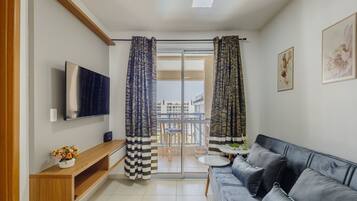 A living room with a sofa, TV, wooden console, and a balcony with curtains.