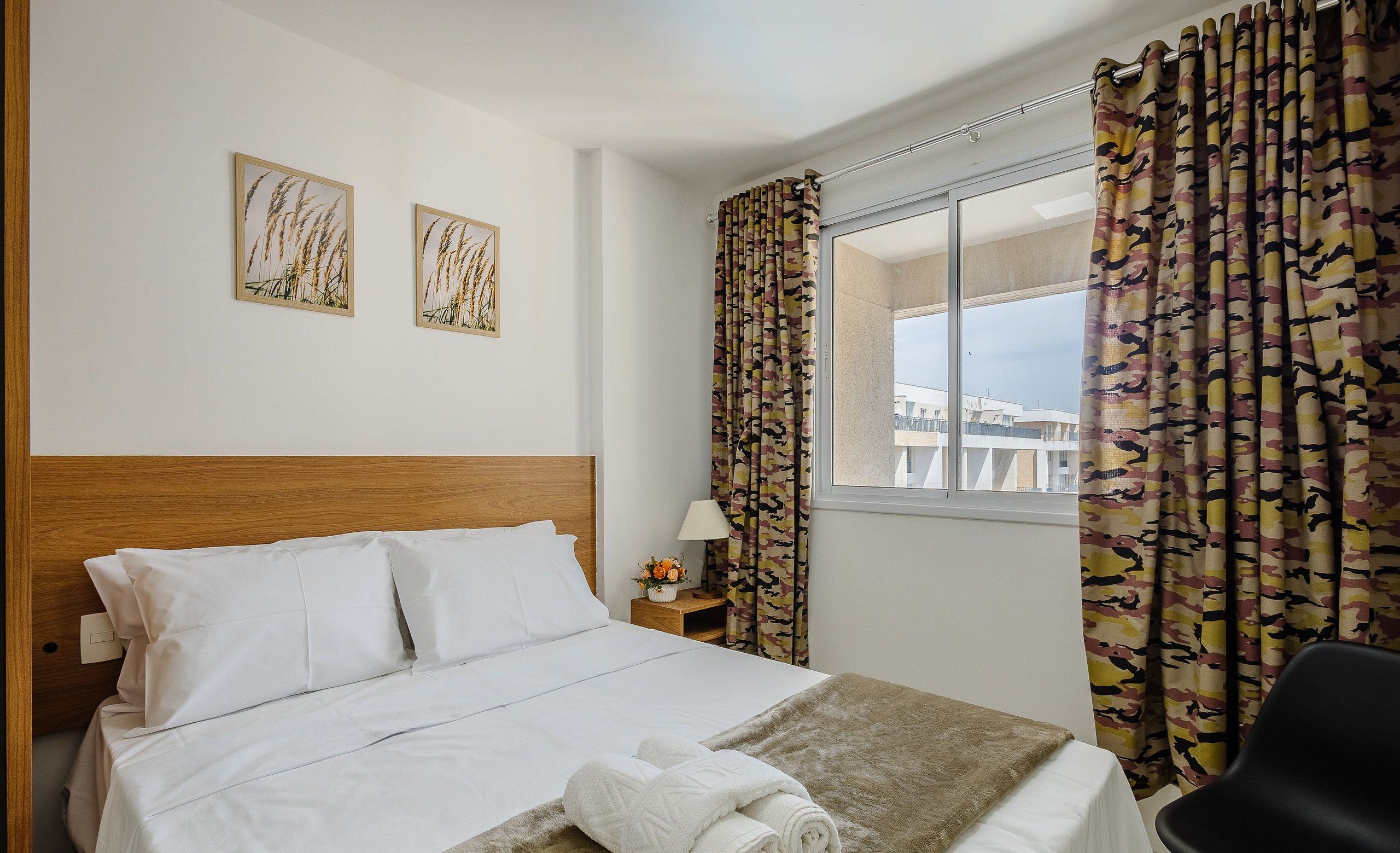 Een hotelkamer met een bed, een nachtkastje met een lamp en een raam met gordijnen.