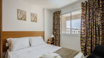 Een hotelkamer met een bed, een nachtkastje met een lamp en een raam met gordijnen.
