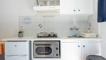Una cucina con forno a incasso, frigorifero e lavello. Si nota un cartello al muro e una pianta sul ripiano.