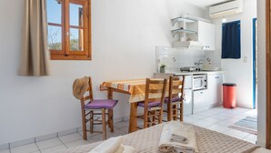A room with a bed, a dining table with chairs, a kitchen area with a microwave, and a window with curtains.