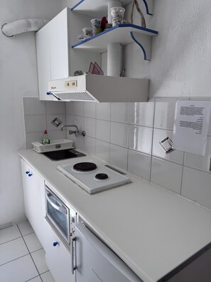 A compact kitchen with a built-in stove, sink, and oven. There are white cabinets, a white countertop, and a blue shelf above the sink. - Studio Apartment '1' with Sea View, Wi-Fi and Air Conditioning (Kea)