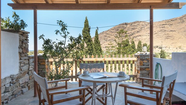Un espace extérieur abrité, doté d’une table et de chaises, de murs en pierre et offrant une vue sur un paysage montagneux.