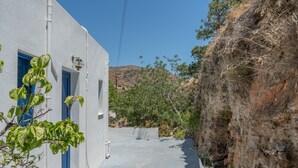 Une ruelle étroite, avec un bâtiment blanc, une porte bleue et une falaise rocheuse.