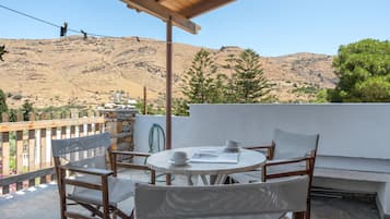 Una terraza con mesa y sillas, una pared blanca y vistas a un paisaje montañoso.