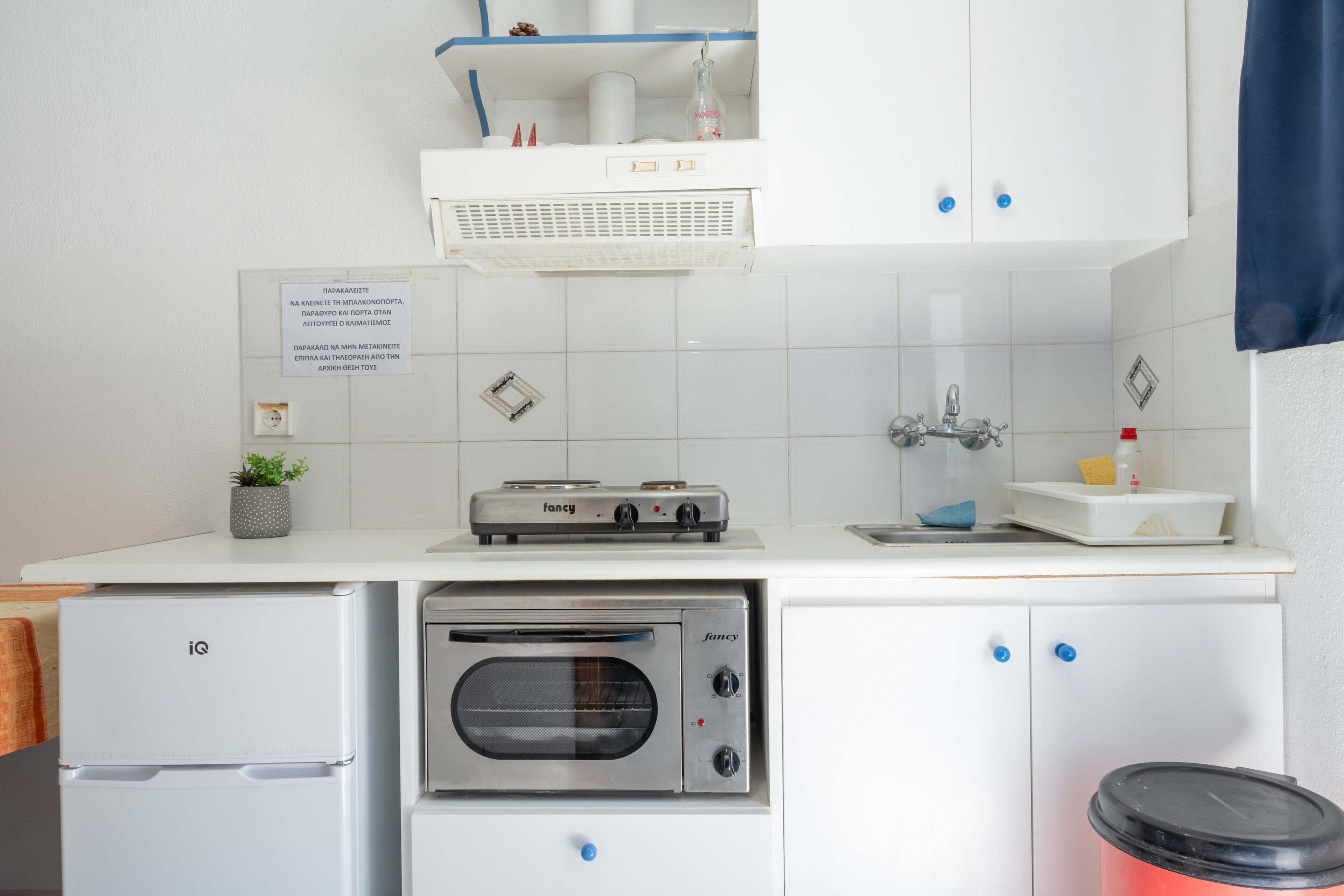 A kitchen with a built-in oven, a refrigerator, and a sink. There is a sign on the wall and a plant on the counter.