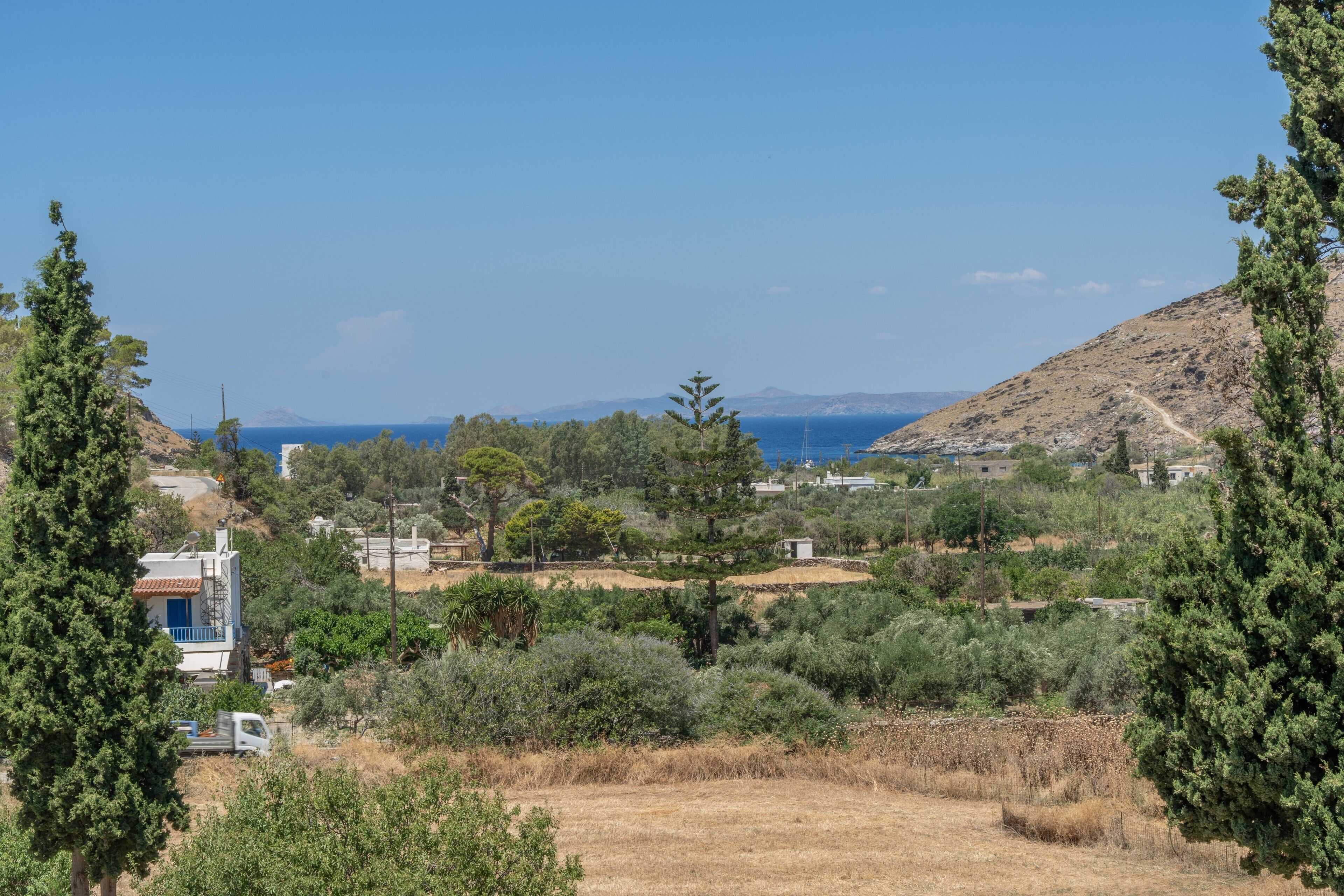 Un paysage rural avec une maison, des arbres et une vue dégagée sur la mer.