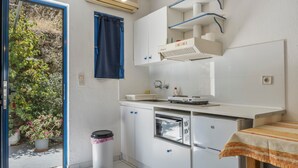 A compact kitchen with a built-in oven, a small countertop, and a window with a blue curtain. - Studio Apartment '5' with Sea View, Wi-Fi and Air Conditioning (Kea)