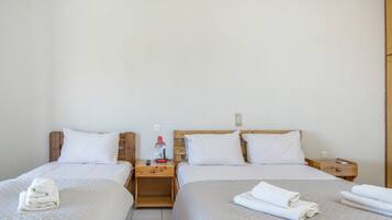 A hotel room with two beds, wooden headboards, white bedding, and a nightstand with a lamp and remote control.