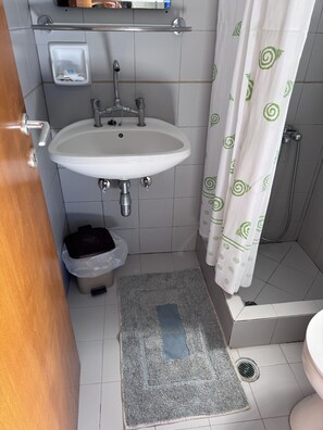 Un baño con lavamanos, ducha y un pequeño cubo de basura.