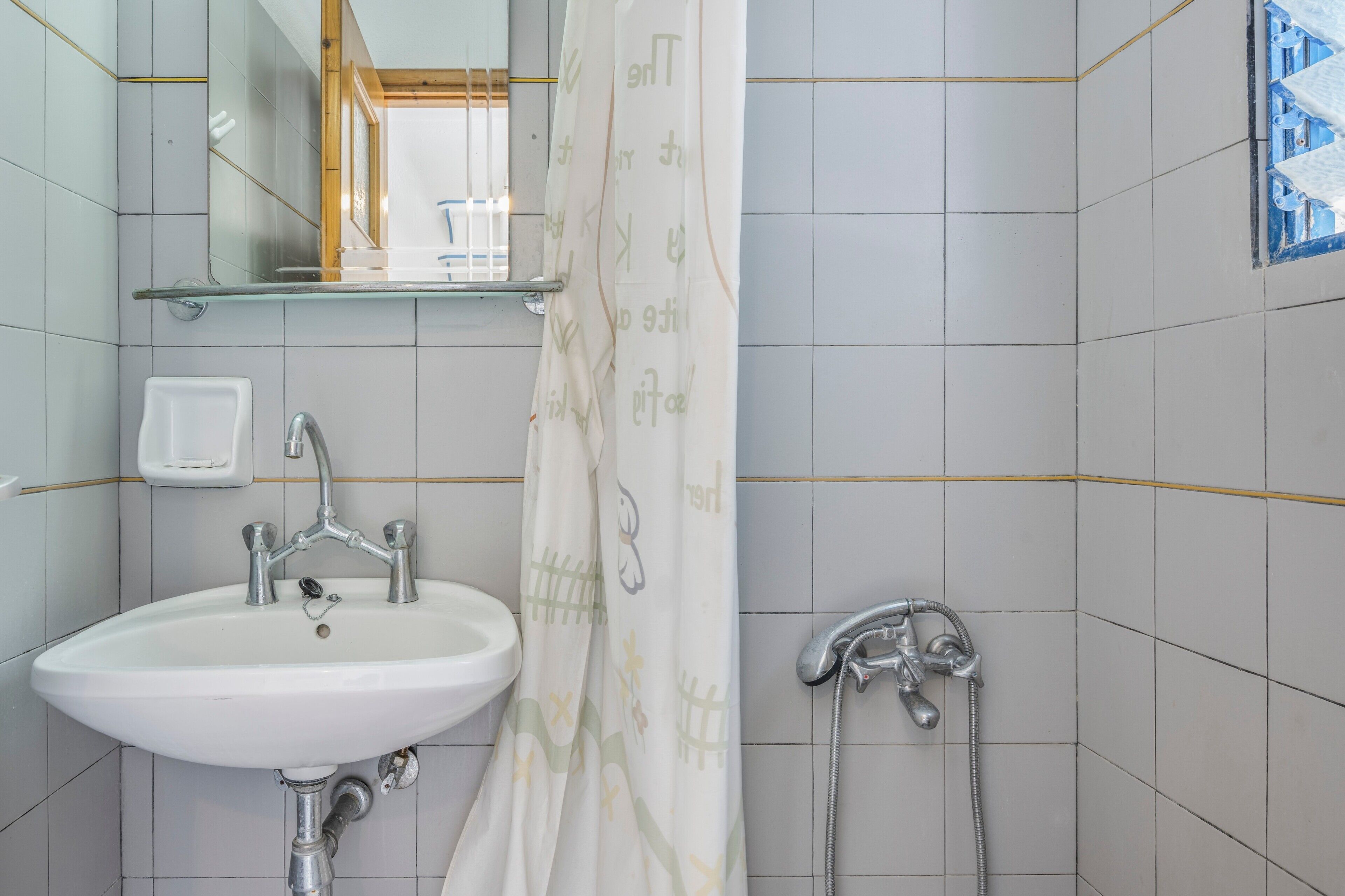 A bathroom with a white sink, a mirror, a shower, and a glass shelf above the sink.