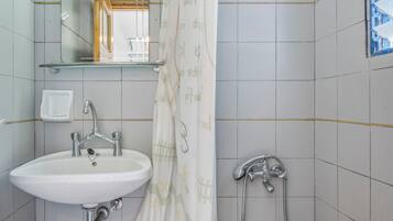 A bathroom with a white sink, a mirror, a shower, and a glass shelf above the sink.