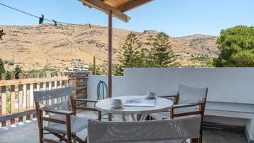 A terrace with a table and chairs, a white wall, and a view of a mountainous landscape.