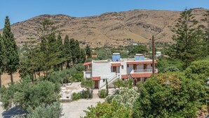 Un bâtiment situé sur une colline, doté de panneaux solaires, entouré d’arbres et avec une chaîne de montagnes en arrière-plan.