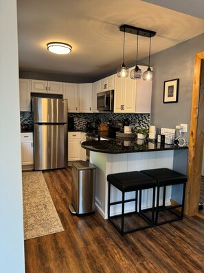 Una cocina moderna con armarios blancos, electrodomésticos de acero inoxidable, encimera negra y suelo de madera.