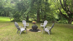 A grassy outdoor area with four Adirondack chairs arranged around a central fire pit. - Beautiful Wine Trail 2-BR Rental (Westfield)