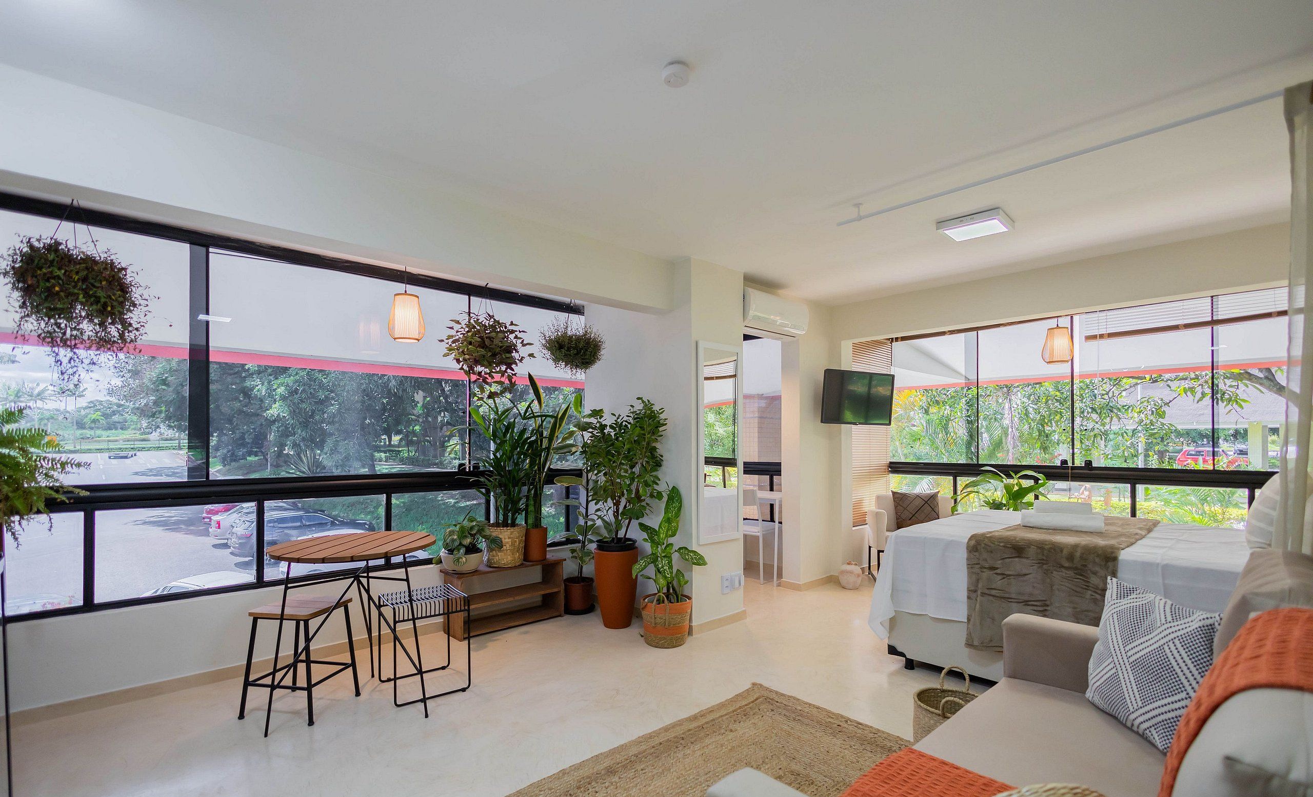 A modern living room with a large window, a sofa, a coffee table, and several potted plants.