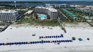 Een resort met een groot zwembad, meerdere gebouwen en een strand voorzien van parasols.