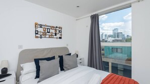 A modern bedroom with a city view, a bed with white bedding, and a unique wall art piece. - Clerkenwell Flat Near Old Street Pet Friendly (London)