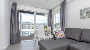 A modern living room with a grey sofa, a colorful pillow, and a dining area with a white chair and table. - Clerkenwell Flat Near Old Street Pet Friendly (London)