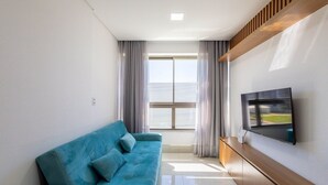 Un soggiorno moderno con un divano blu, una televisione a schermo piatto montata sulla parete e un'ampia finestra con tende.