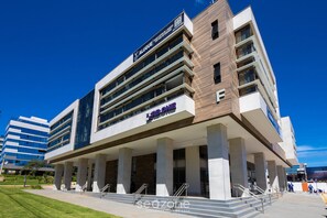 Un edificio moderno con un llamativo letrero que dice 'Alugue', varios pisos y el logotipo de 'KBBONE'.