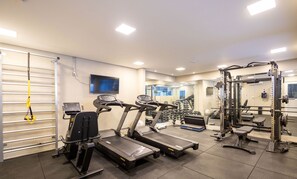 Un gimnasio con cintas de correr, máquinas de pesas y un muro de espejos.