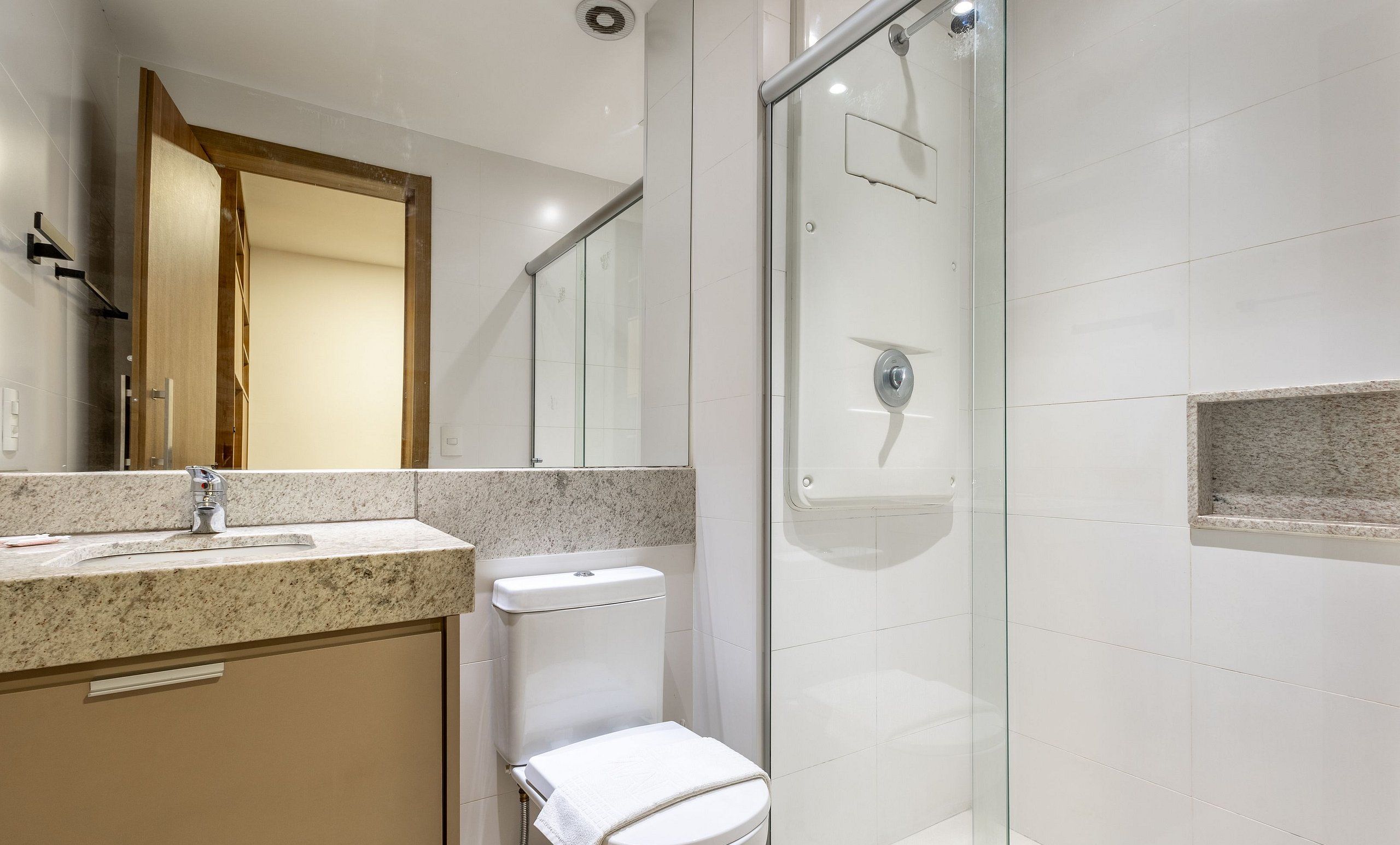 Un baño moderno con encimera de granito, inodoro, cabina de ducha de vidrio y espejo con marco de madera.