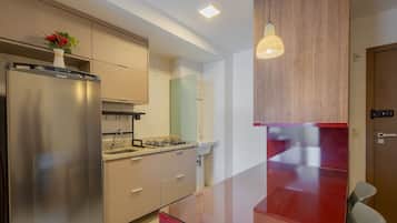 A modern kitchen with a stainless steel refrigerator, a gas stove, and a built-in oven. There is a wooden cabinet above the stove and a red countertop.