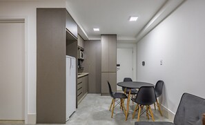 A modern kitchen with a built-in microwave, a refrigerator, and a dining area with a round table and four chairs. - Full Apartment in Setor Noroeste Eme0218 (Brasília)