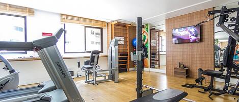 A gym with treadmills, weight machines, and a TV on the wall.