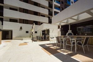 An outdoor seating area with tables and chairs, a covered section, and a building with multiple floors and balconies. - Well-located apt in Aguas Claras Rmh1511 (Águas Claras)