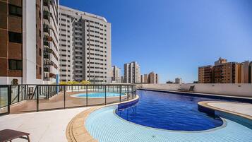 Una piscina en la azotea con barandilla de cristal, rodeada de edificios altos.