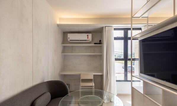 Un salon moderne avec une table basse en verre, un canapé gris, un système de climatisation intégré et une vue sur l’extérieur grâce à une grande fenêtre.